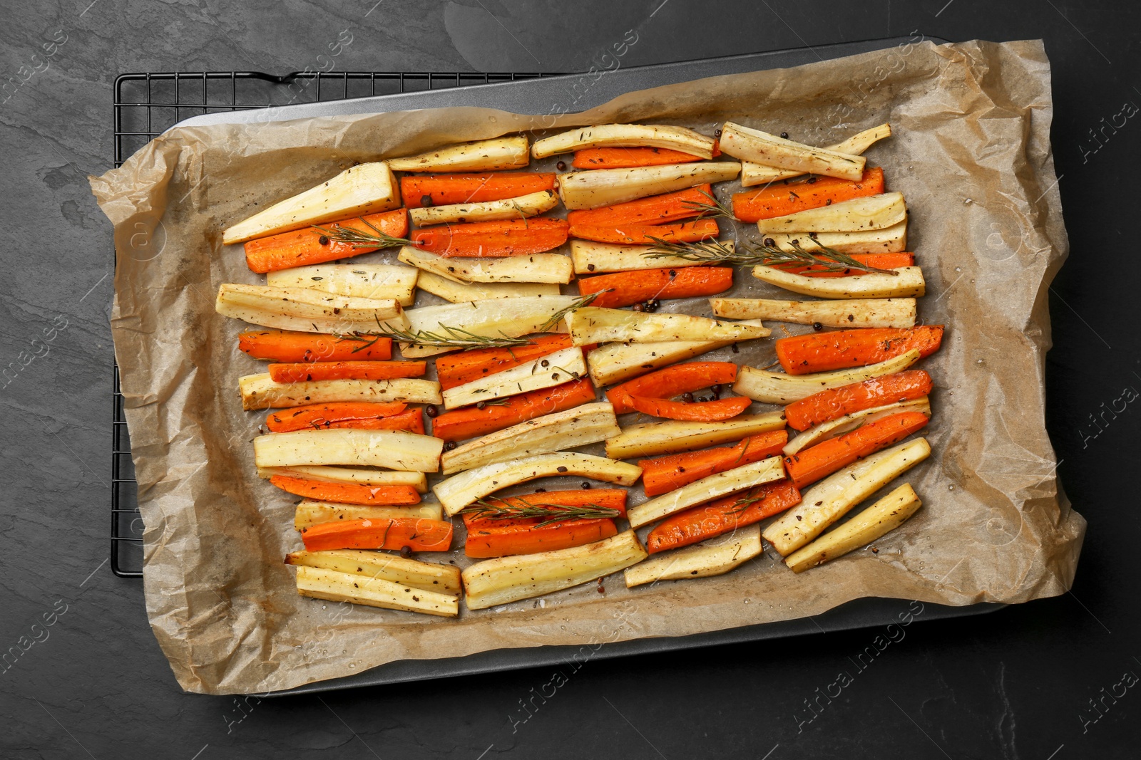 Photo of Tray with baked parsnips and carrots on black table, top view