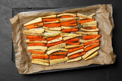 Tray with baked parsnips and carrots on black table, top view