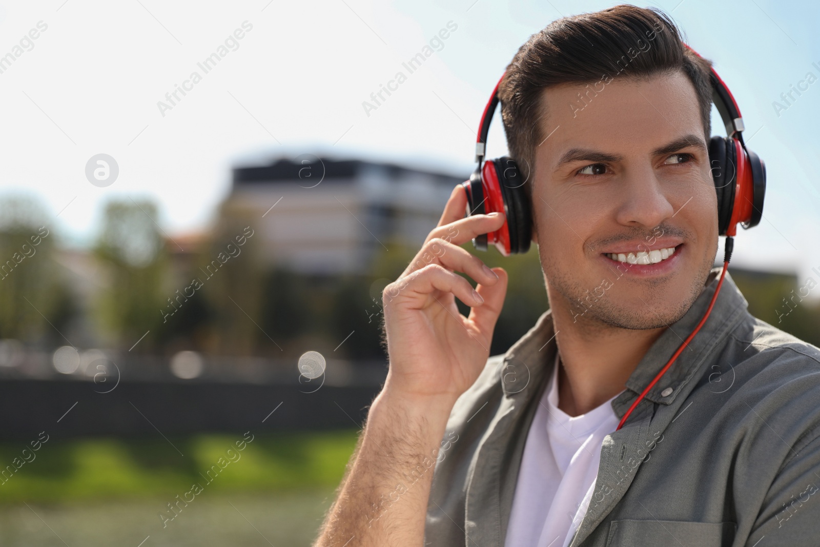 Photo of Handsome man with headphones listening to music outdoors on sunny day, space for text