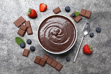 Photo of Delicious chocolate cream with berries and mint on grey table, flat lay