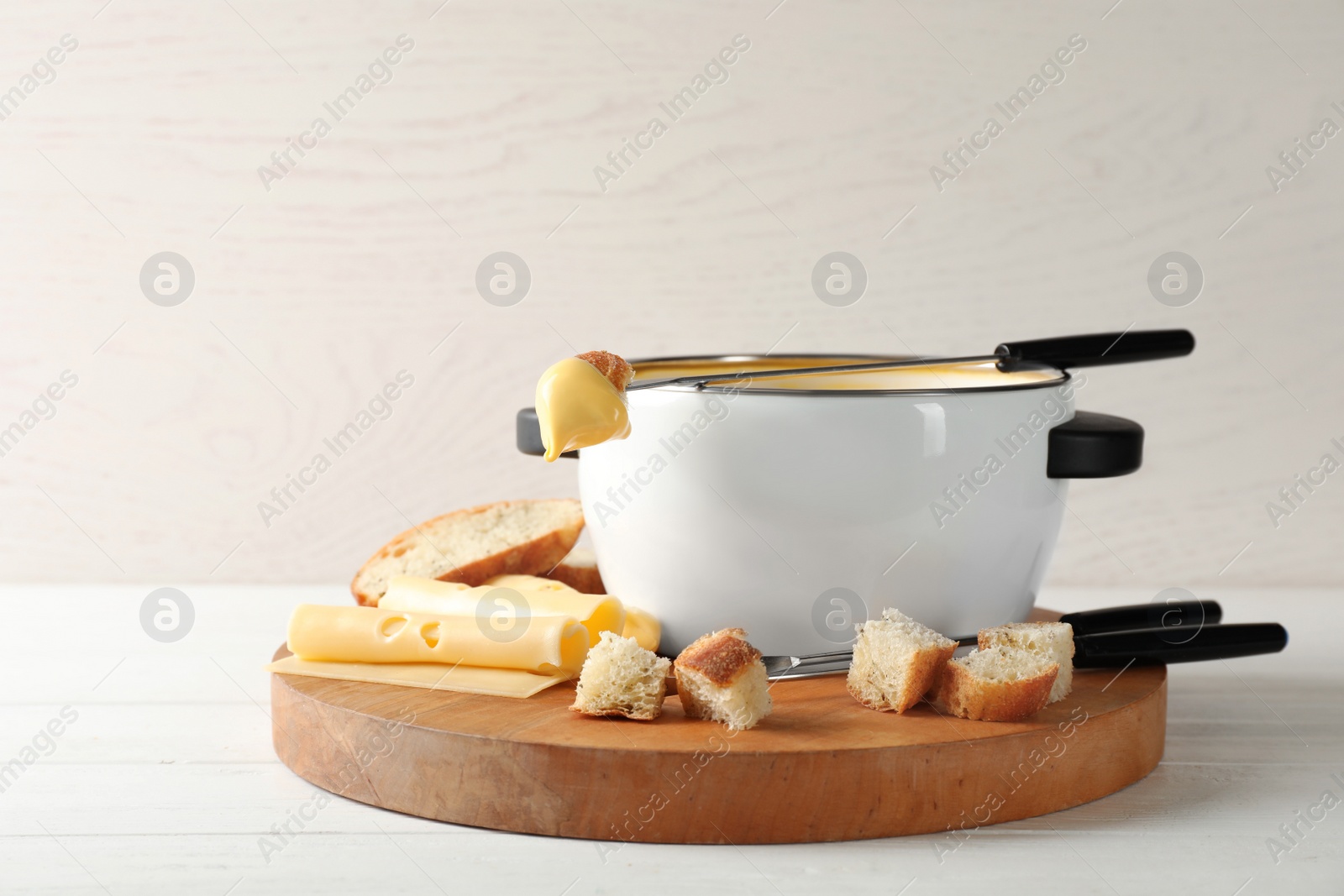 Photo of Pot of delicious cheese fondue and fork with bread on wooden table