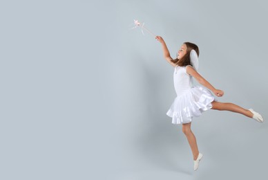 Photo of Cute little girl in fairy costume with wings and magic wand on light background. Space for text