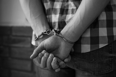 Photo of Criminal detained in handcuffs against wall, closeup. Black and white effect