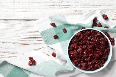 Photo of Tasty dried cranberries in bowl on white wooden table, flat lay. Space for text