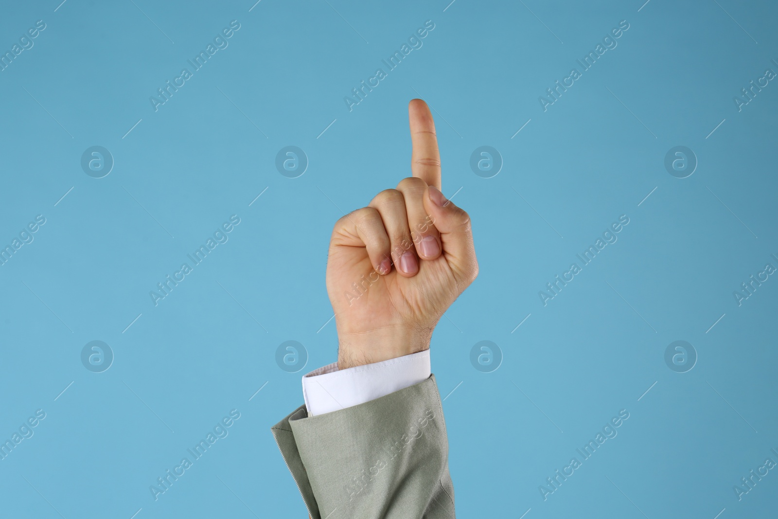 Photo of Businessman pointing at something on light blue background, closeup. Finger gesture