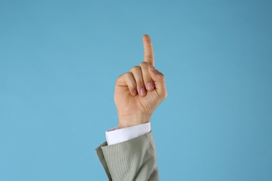 Businessman pointing at something on light blue background, closeup. Finger gesture