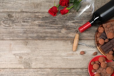 Photo of Bottle of red wine, glass, chocolate sweets, corkscrew and roses on wooden table, above view. Space for text