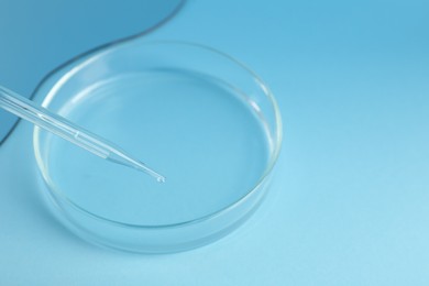 Empty petri dish and pipette on light blue background, closeup. Space for text