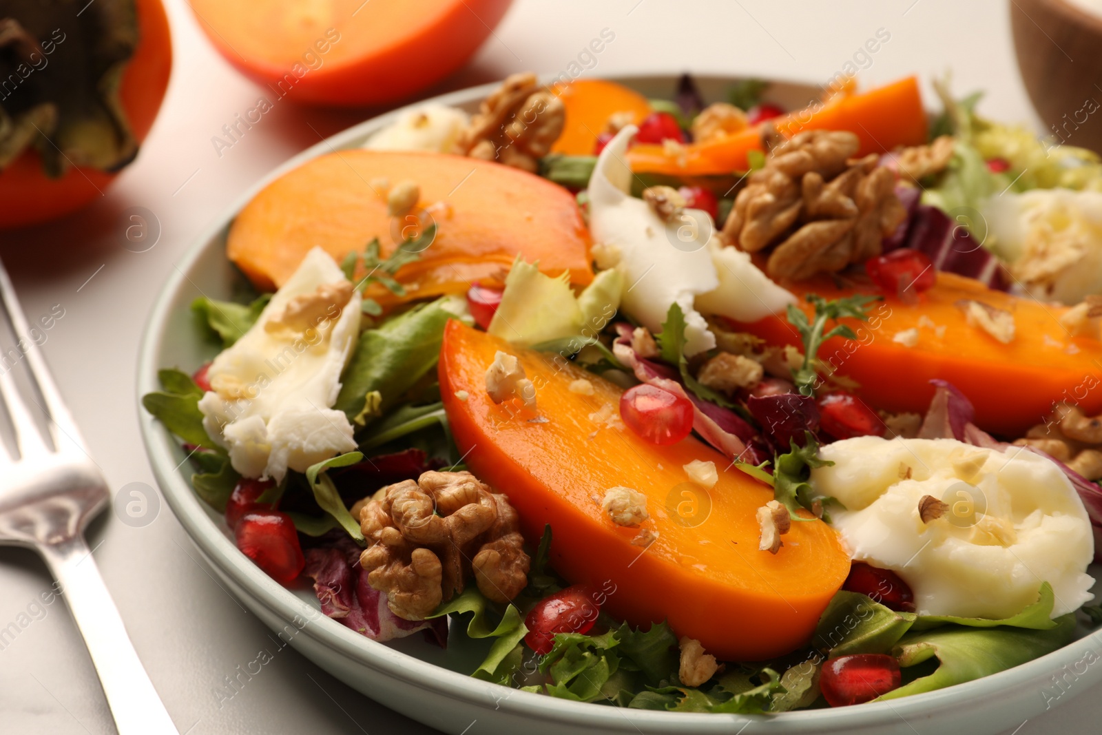Photo of Delicious persimmon salad with cheese and pomegranate served on white table, closeup