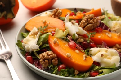 Delicious persimmon salad with cheese and pomegranate served on white table, closeup