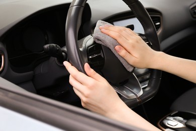 Photo of Woman cleaning steering wheel with rag in car, closeup