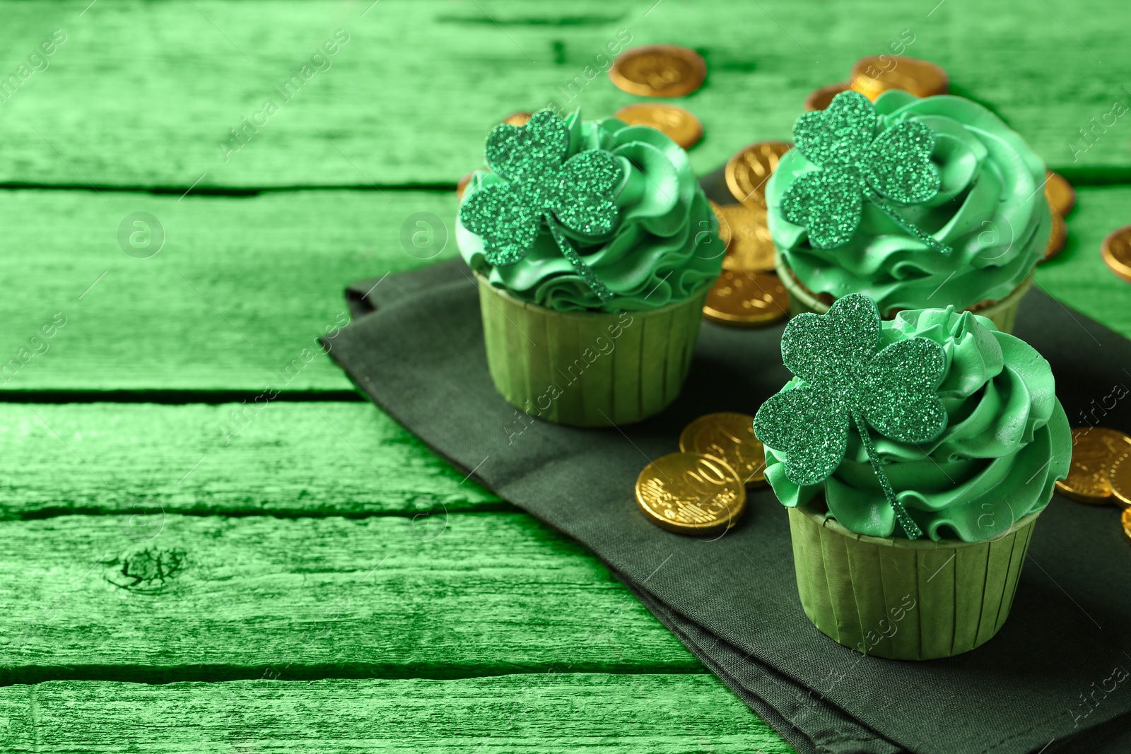 Image of St. Patrick's day. Tasty cupcakes with clover leaf toppers and cream on green wooden table, closeup. Space for text