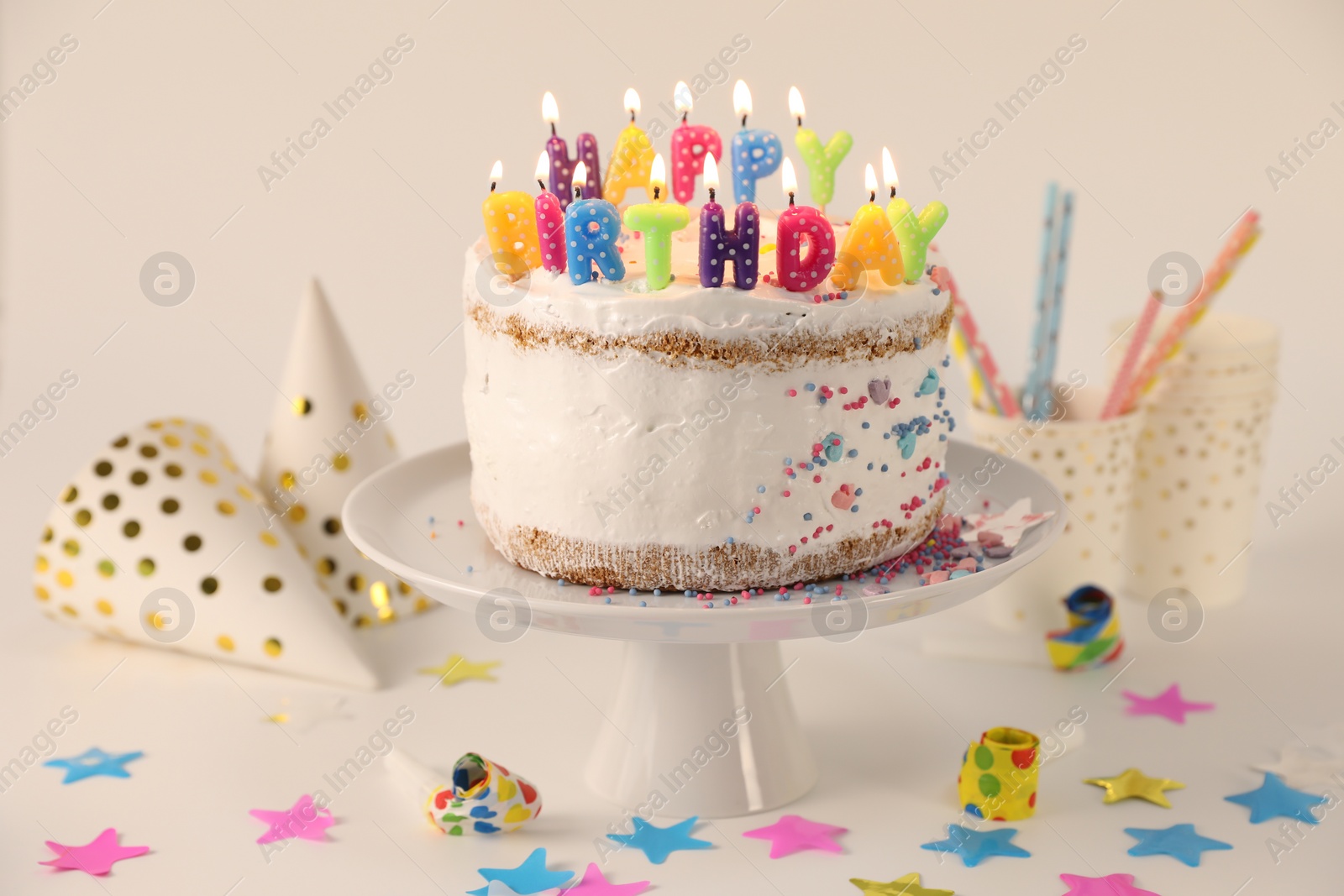 Photo of Tasty Birthday cake with burning candles and party decor on white table