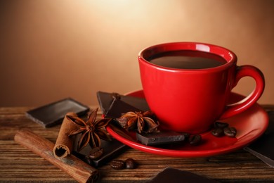 Photo of Cup of delicious hot chocolate, spices and coffee beans on wooden table. Space for text