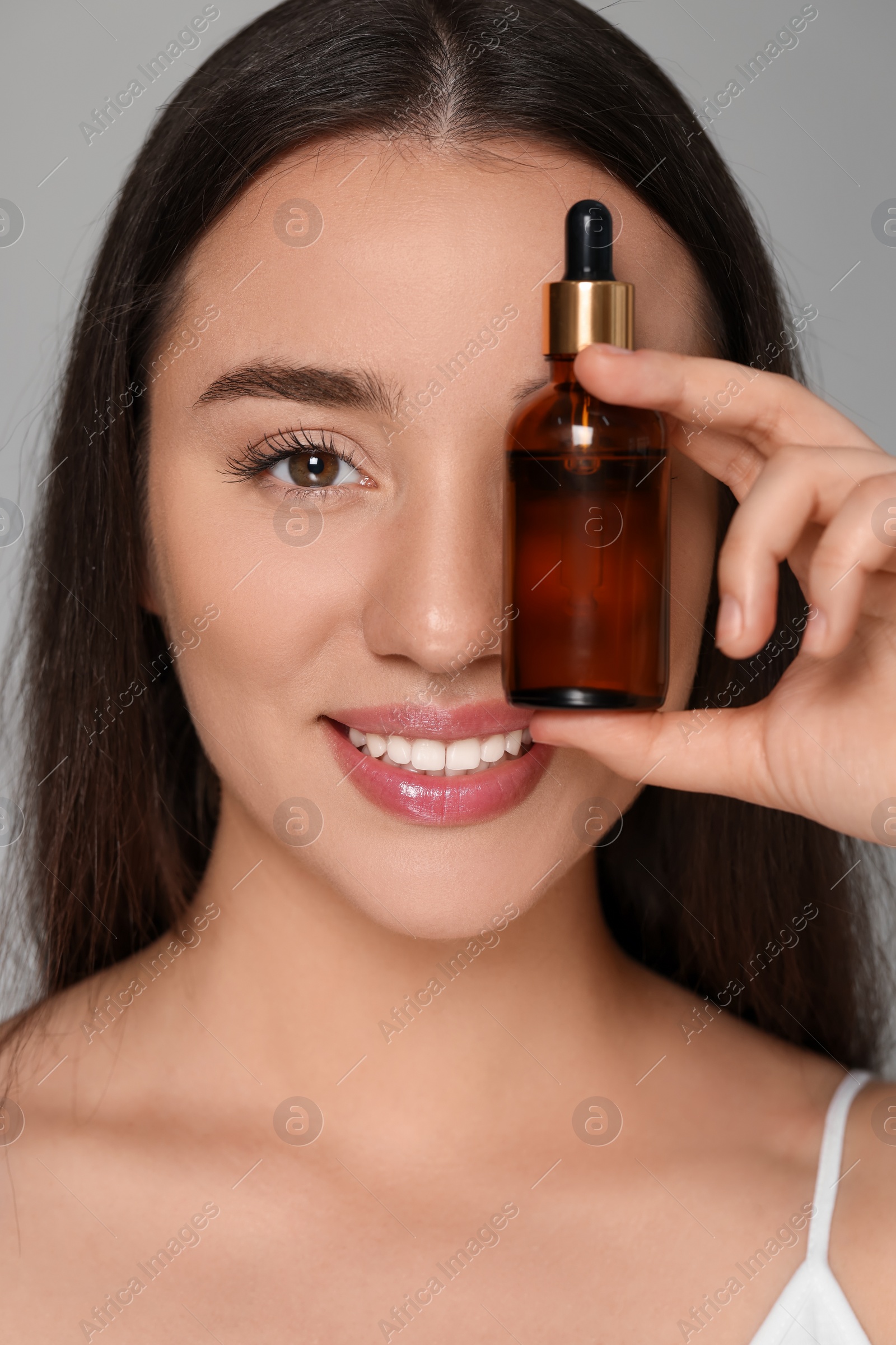 Photo of Beautiful young woman with essential oil on light grey background, closeup