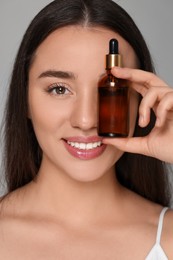 Beautiful young woman with essential oil on light grey background, closeup