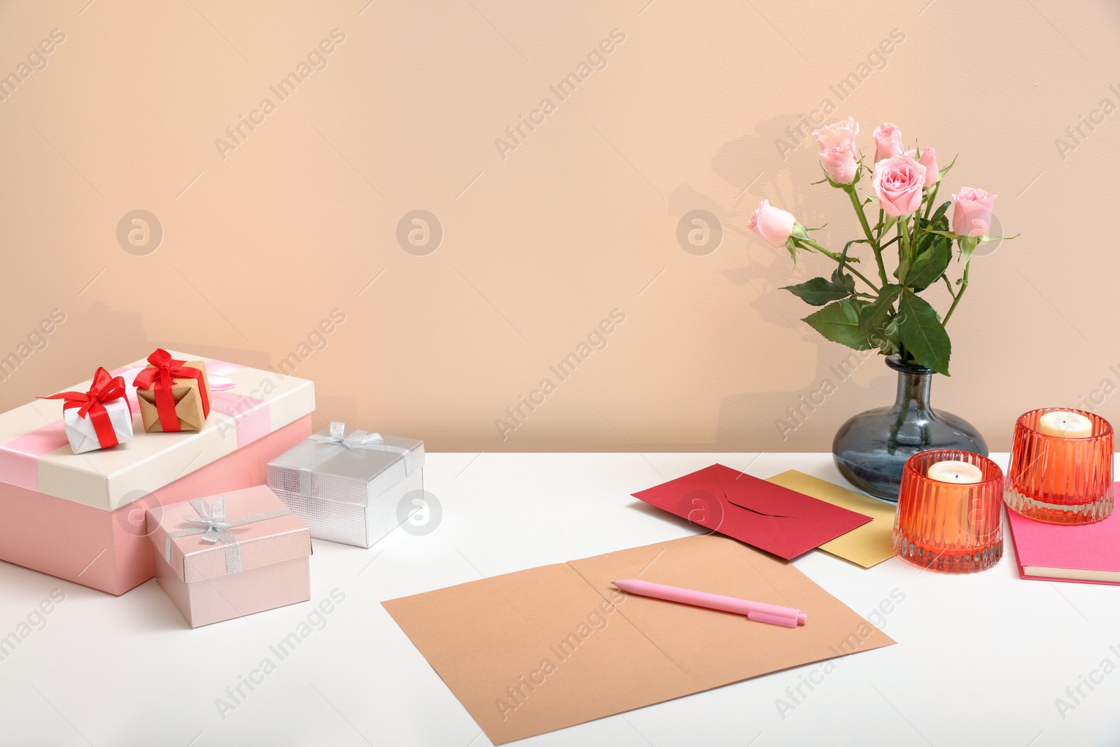 Photo of Greeting card, flowers and candles on white table indoors