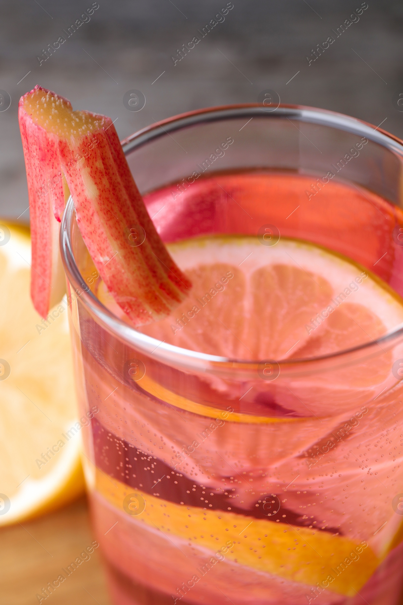 Photo of Glass of tasty rhubarb cocktail with lemon on board, closeup
