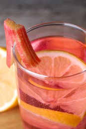 Glass of tasty rhubarb cocktail with lemon on board, closeup
