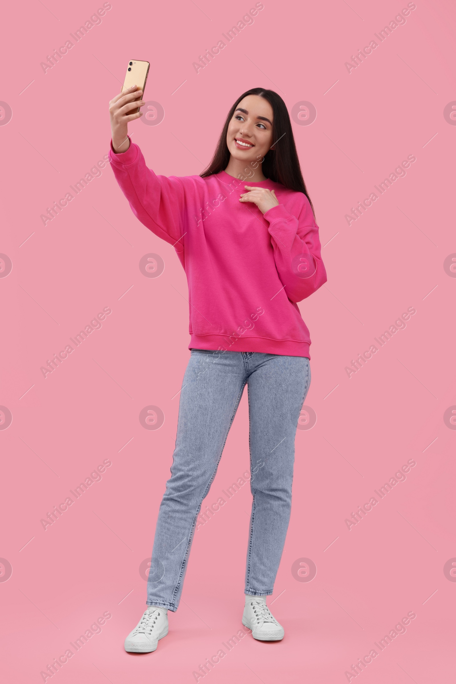 Photo of Smiling young woman taking selfie with smartphone on pink background