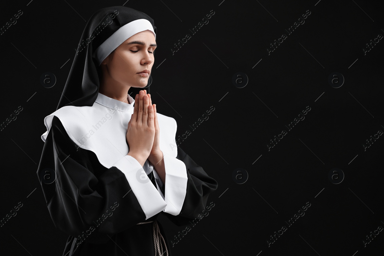 Photo of Nun with clasped hands praying to God on black background. Space for text