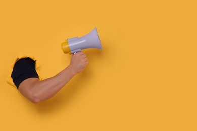 Photo of Special promotion. Man holding megaphone through hole in orange paper, closeup. Space for text