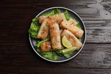 Photo of Tasty fried spring rolls, lettuce and lime on wooden table, top view