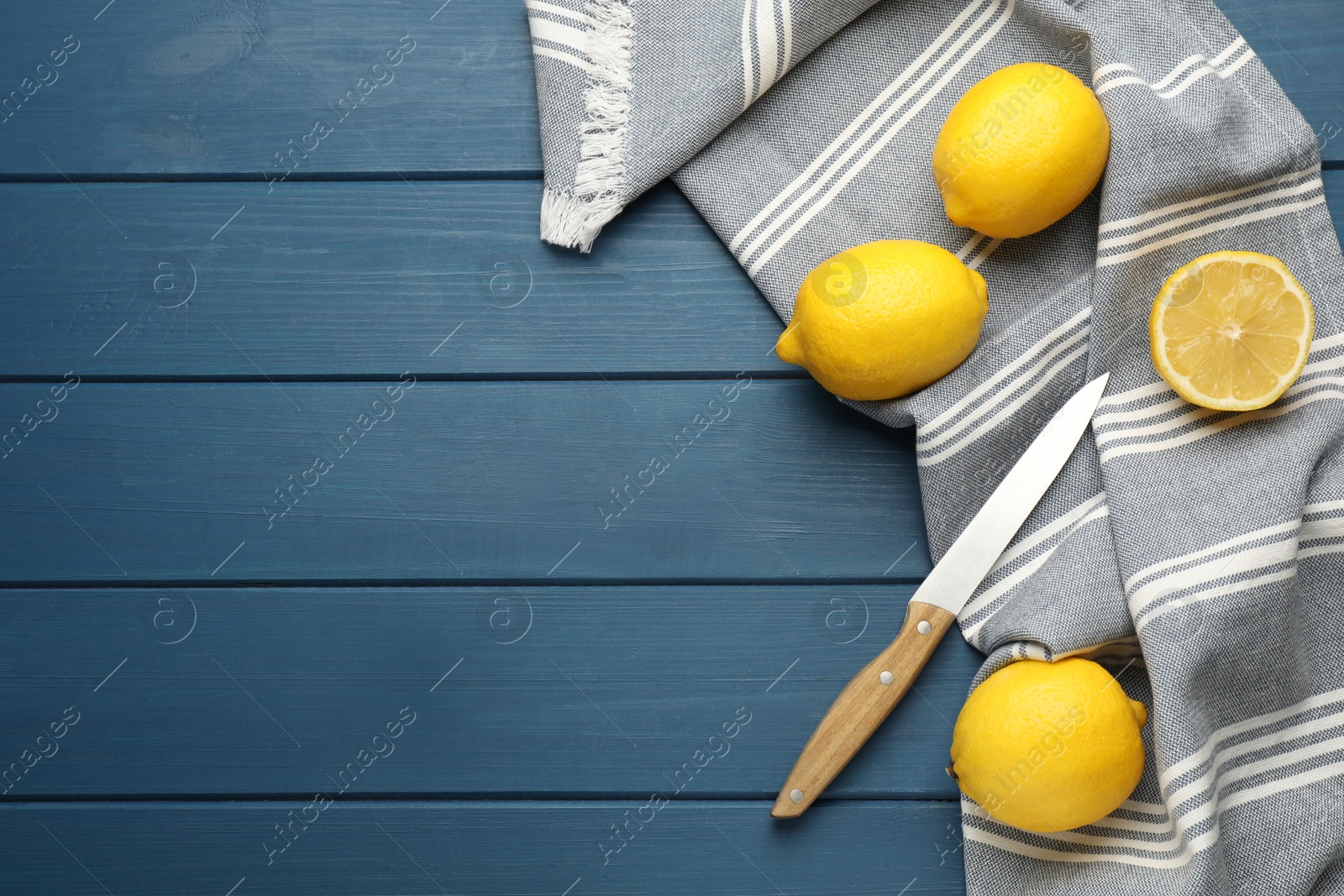 Photo of Striped kitchen towel, lemons and knife on blue wooden table, flat lay. Space for text