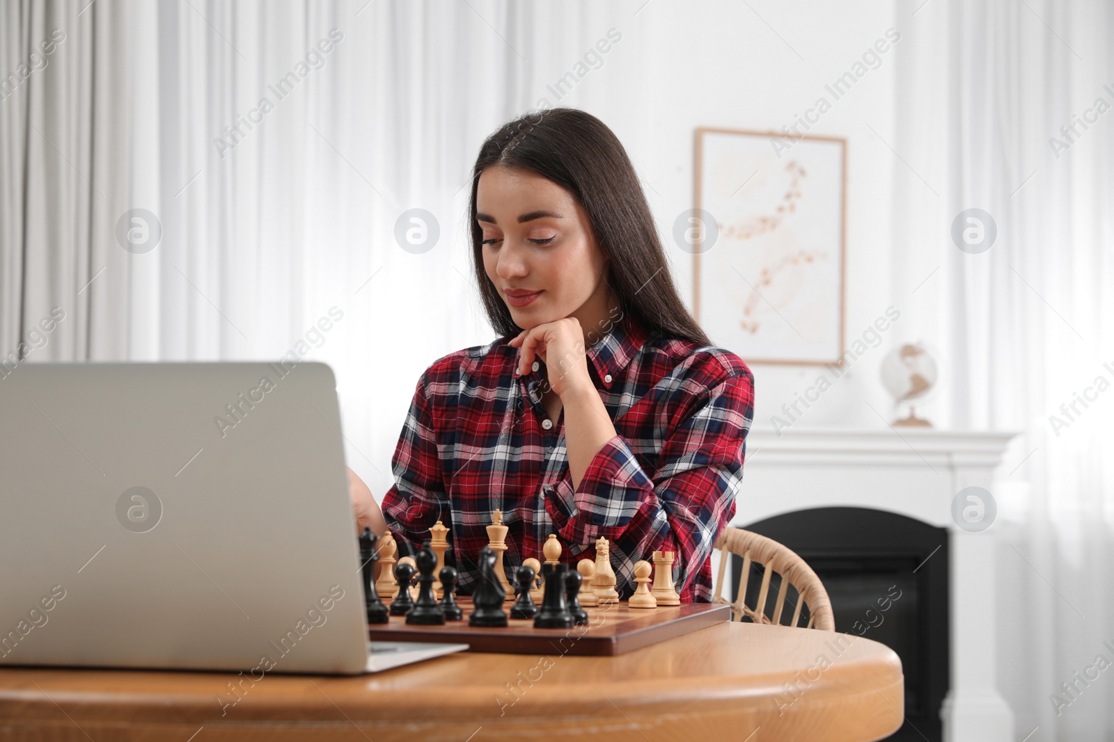 Photo of Young woman playing chess with partner through online video chat at home