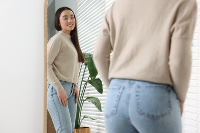 Young woman in stylish jeans near mirror indoors