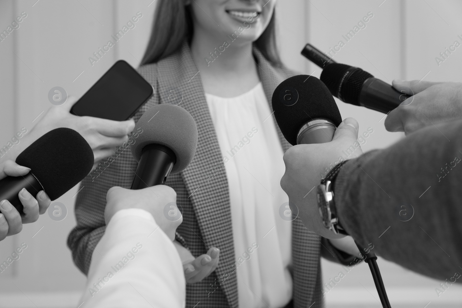 Image of Businesswoman giving interview to journalists indoors, closeup. Black and white effect