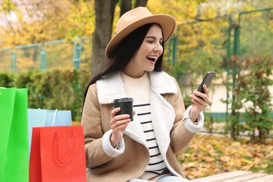 Special Promotion. Emotional young woman with smartphone and cup of drink in park