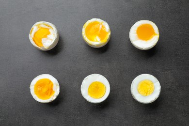 Photo of Different readiness stages of boiled chicken eggs on dark grey table, flat lay