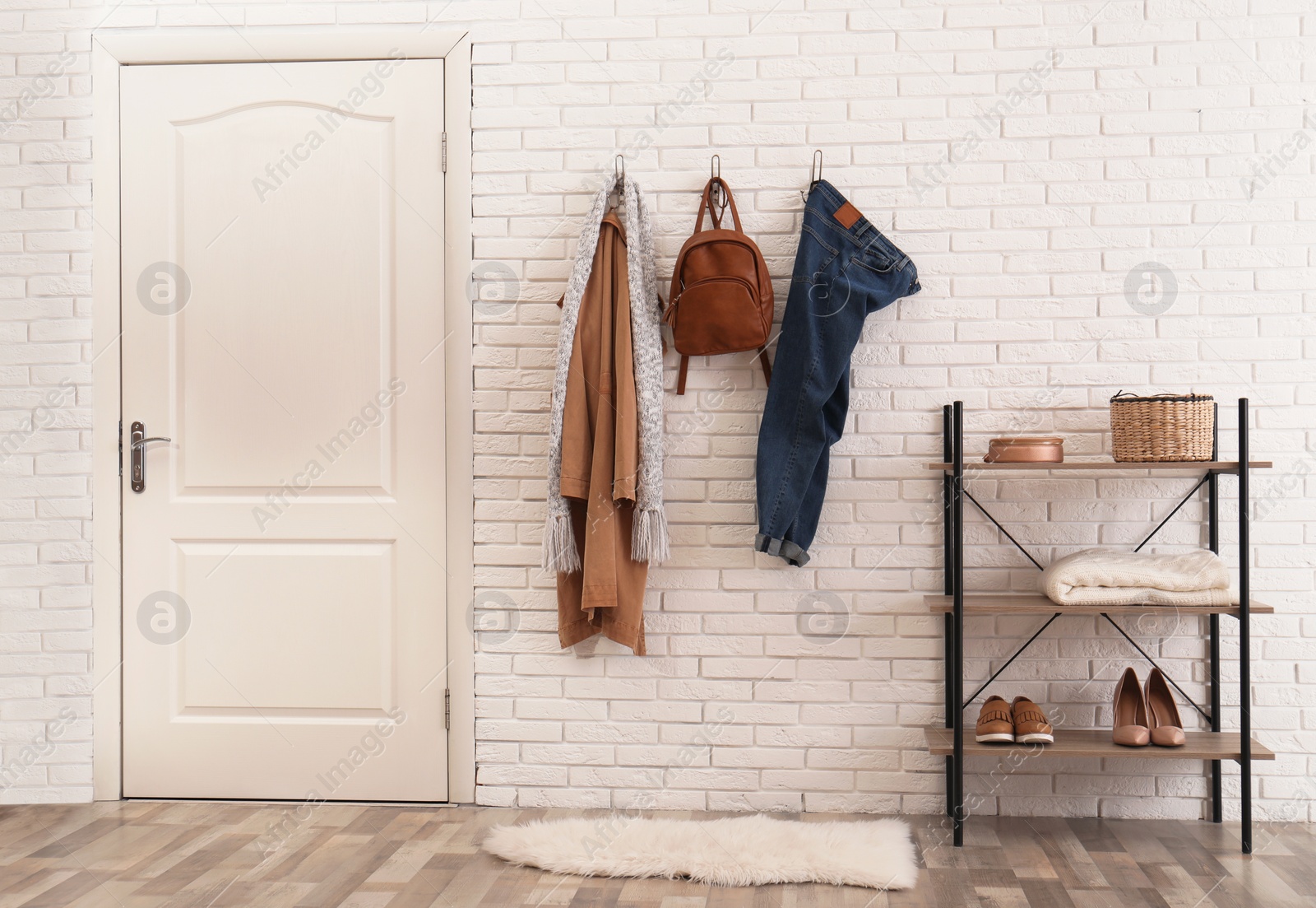 Photo of Stylish hallway interior with door, comfortable furniture and clothes on brick wall