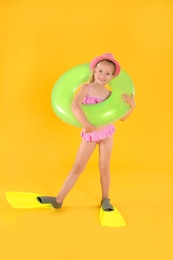 Photo of Cute little child in beachwear with bright inflatable ring on yellow background