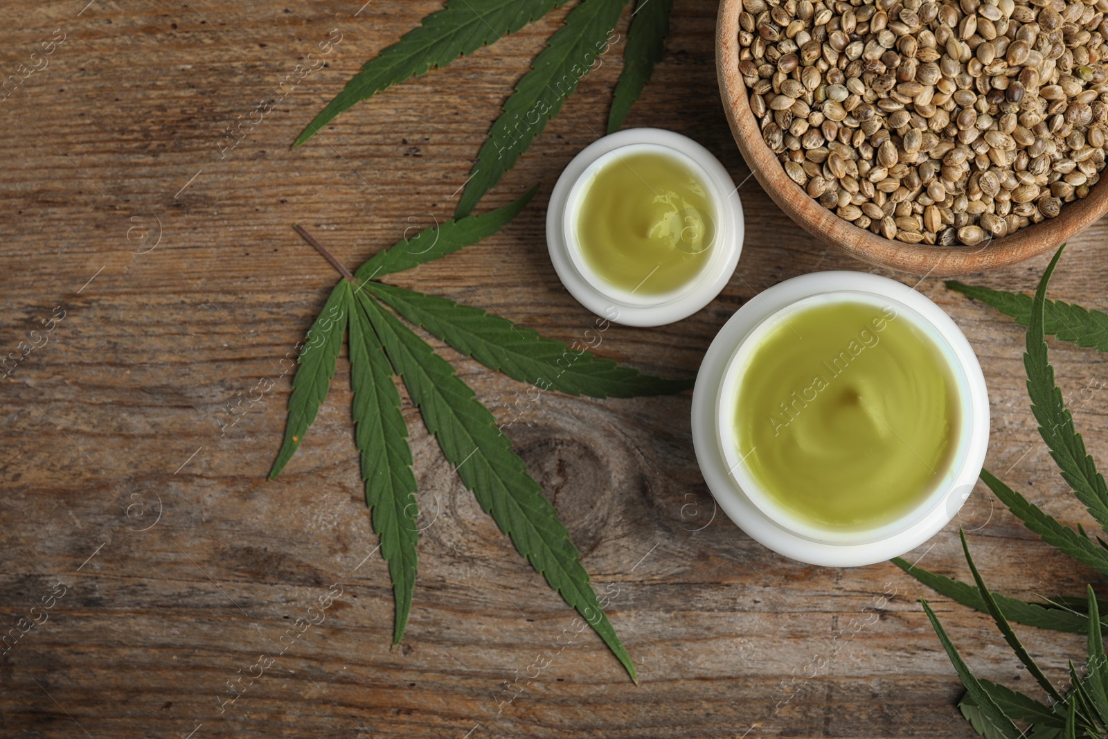 Photo of Jars of hemp cream and seeds on wooden table, flat lay with space for text. Organic cosmetics