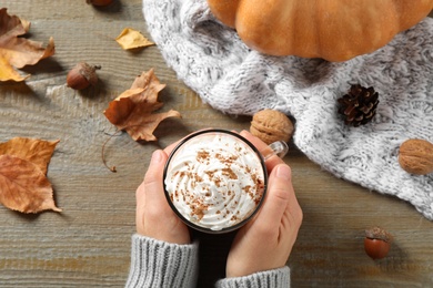 Photo of Woman with cup of pumpkin spice latte at wooden table, top view