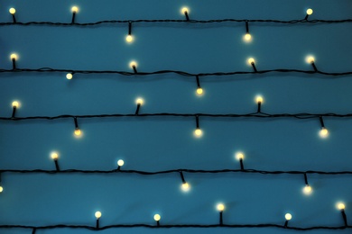 Glowing Christmas lights on blue background, top view