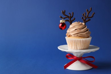 Tasty cupcake with chocolate reindeer antlers and Christmas bauble on blue background, space for text