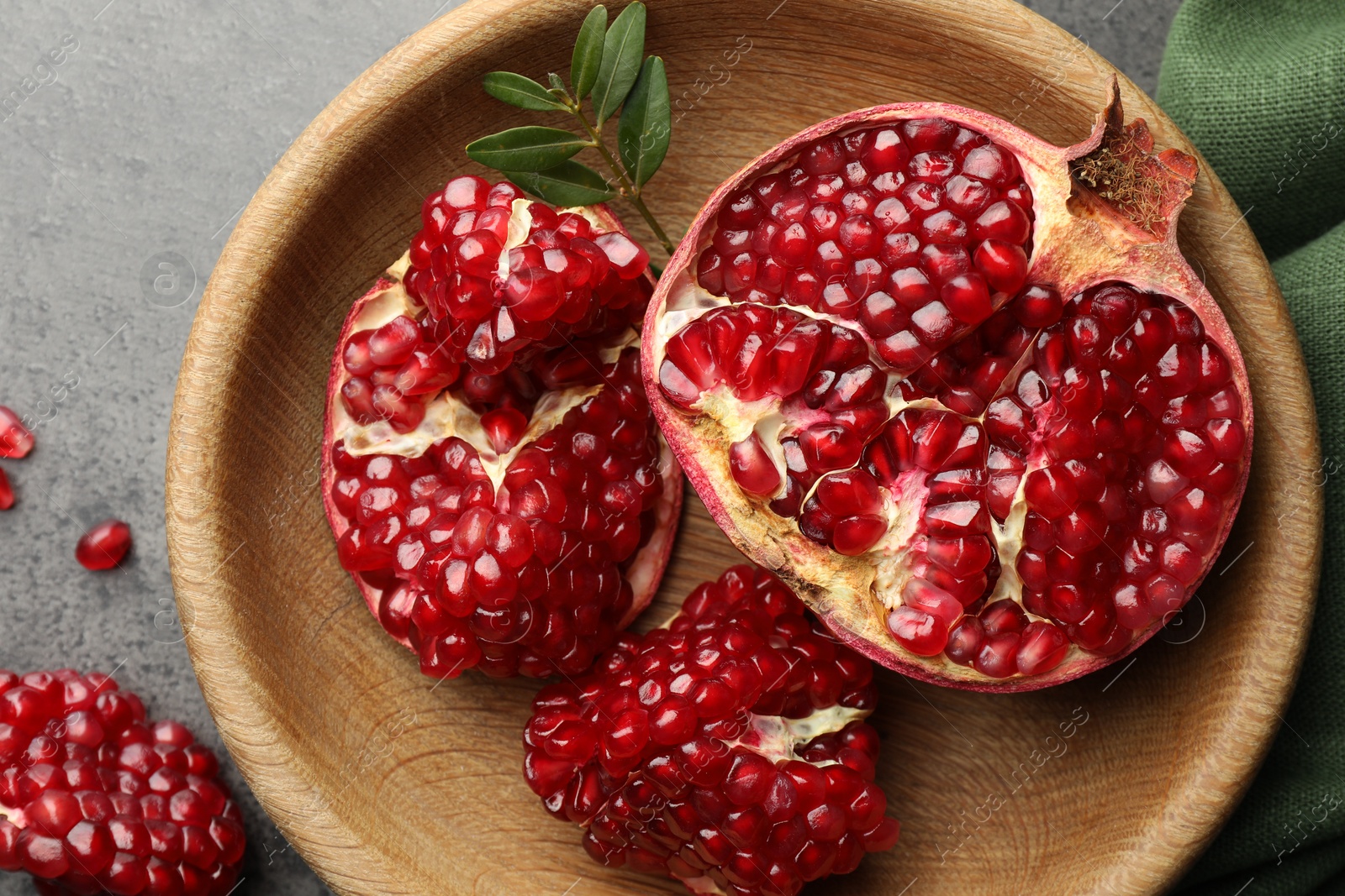 Photo of Cut fresh pomegranate and green leaves on grey table, top view