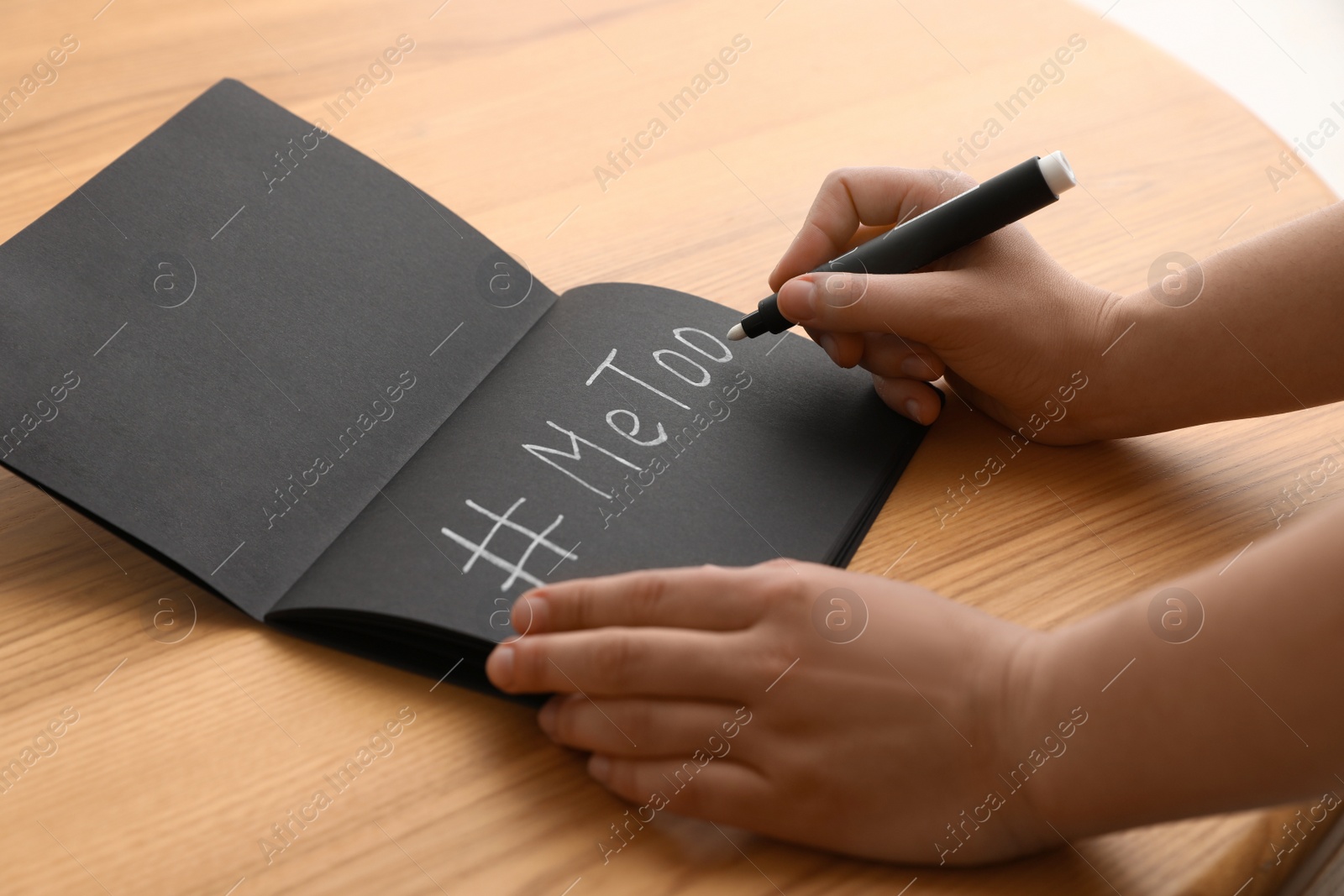 Photo of Woman writing hashtag MeToo in notebook at table, closeup. Stop sexual assault