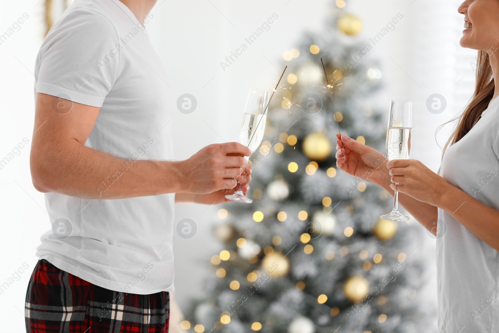 Photo of Happy young couple with glasses of champagne and sparklers at home. Christmas celebration