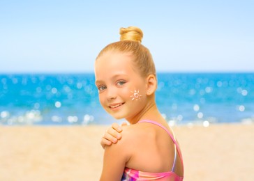 Image of Sun protection. Cute girl applying sunblock onto skin on beach