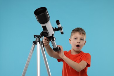 Surprised little boy with telescope on light blue background