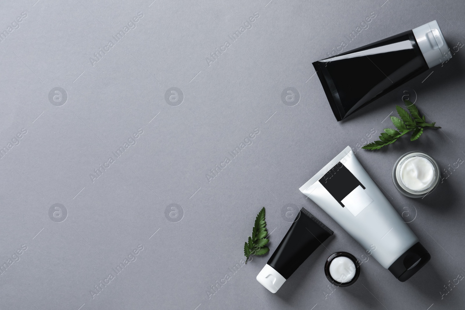 Photo of Tubes and jars of men's facial cream on light grey background, flat lay. Space for text