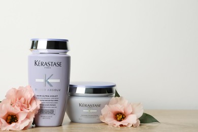 Photo of MYKOLAIV, UKRAINE - SEPTEMBER 07, 2021: Kerastase hair care cosmetic products and beautiful flowers on wooden table. Space for text