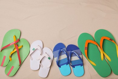 Different bright flip flops on sand, flat lay. Space for text