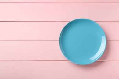 Clean light blue plate on pink wooden table, top view. Space for text