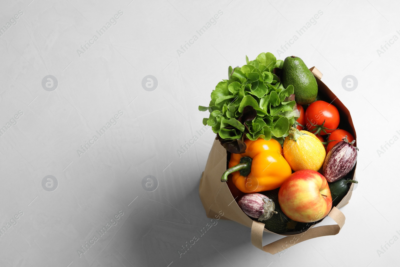Photo of Paper bag full of fresh vegetables and fruits on light background, top view. Space for text