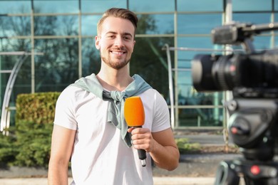 Photo of Young male journalist with microphone working on city street